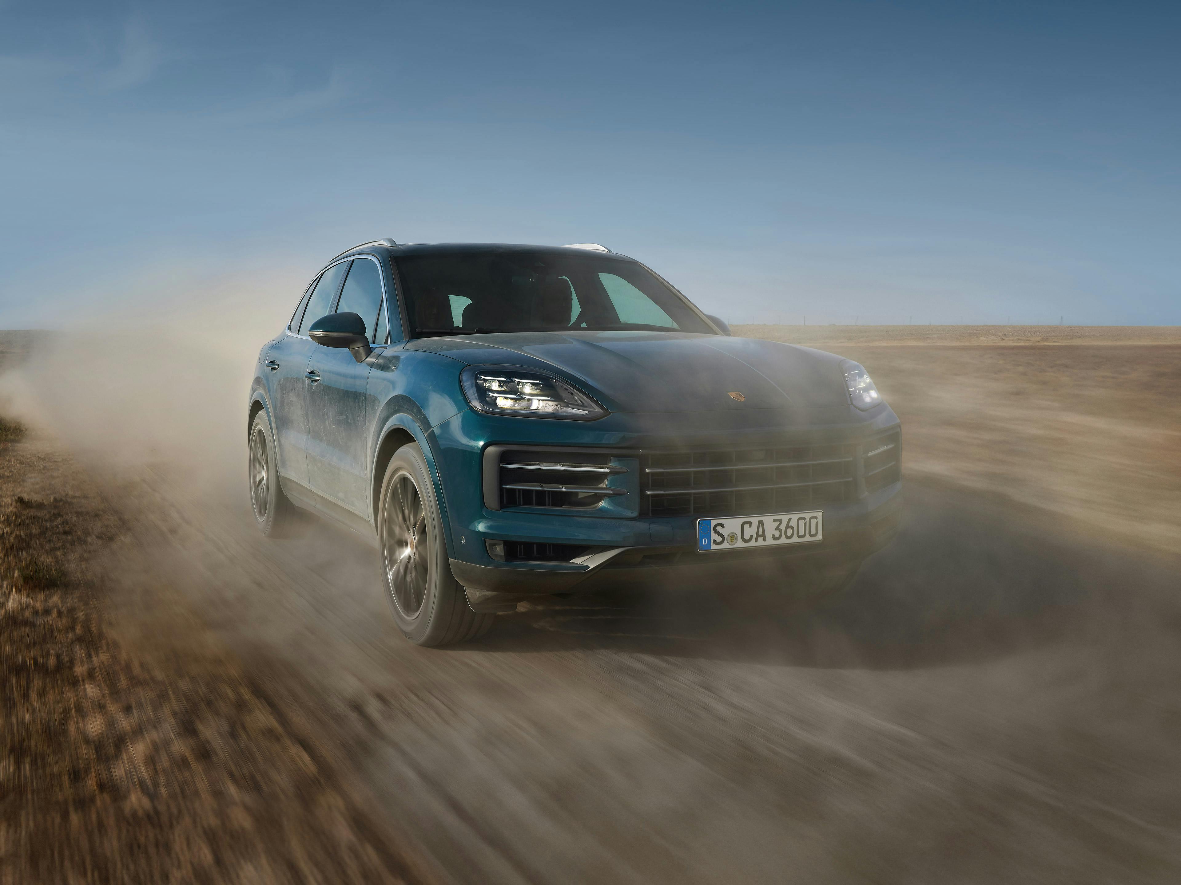 A blue Porsche Cayenne driving on a dusty desert road. 