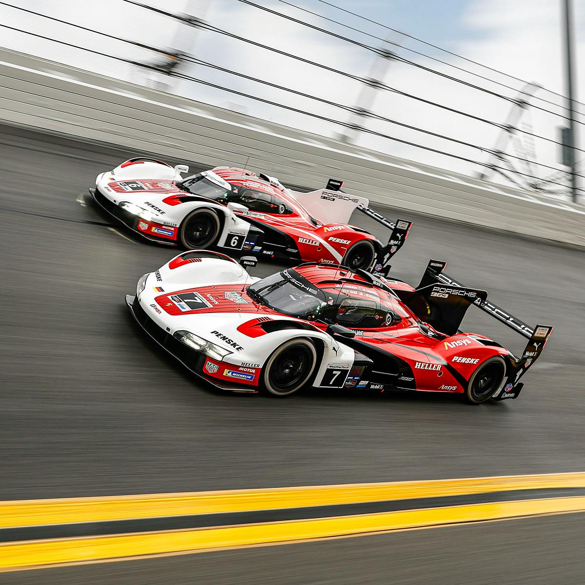 Two red and white Porsche 963 cars racing side by side in a circuit