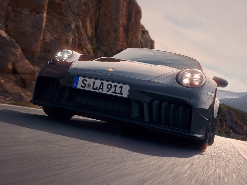 Porsche 911 Carrera GTS in Slate Grey Neo driving on a road. Front view from the front.