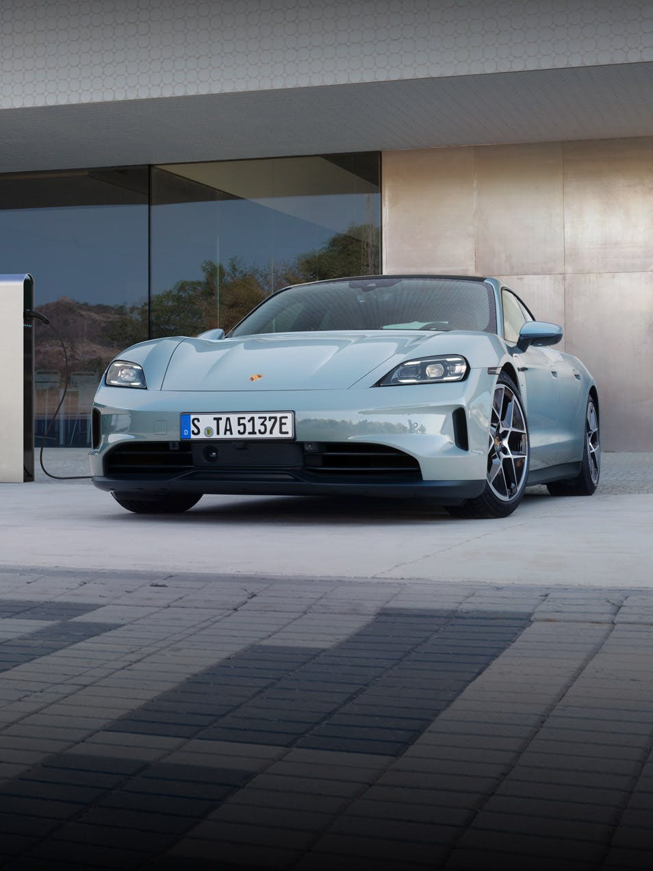 The new Porsche Taycan parked outside in front of a modern building. 